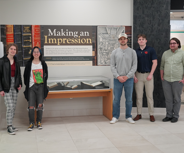 4 students stand around their display case, two on the left and two on the right, instructor next to students on the right