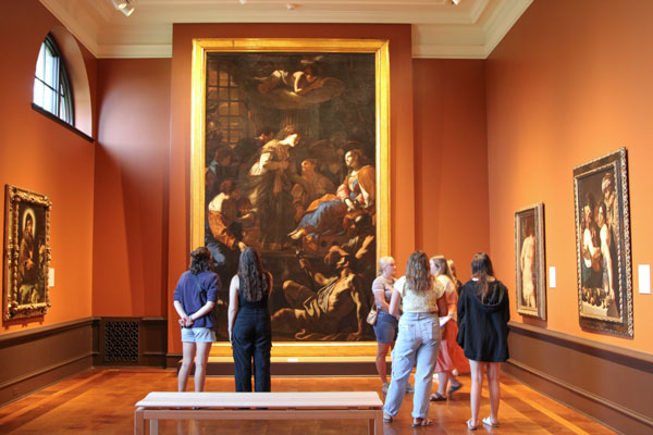 Group of students stare at paintings, including one piece that is about 15 feet tall.