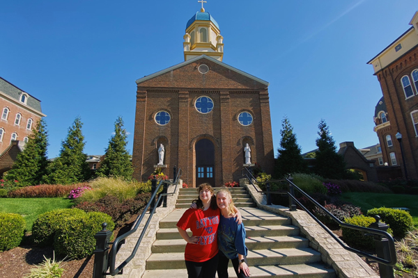 Two women pose in front of the Chapel of the Immaculate Conception. One woman wears a Dayton Flyers shirt.