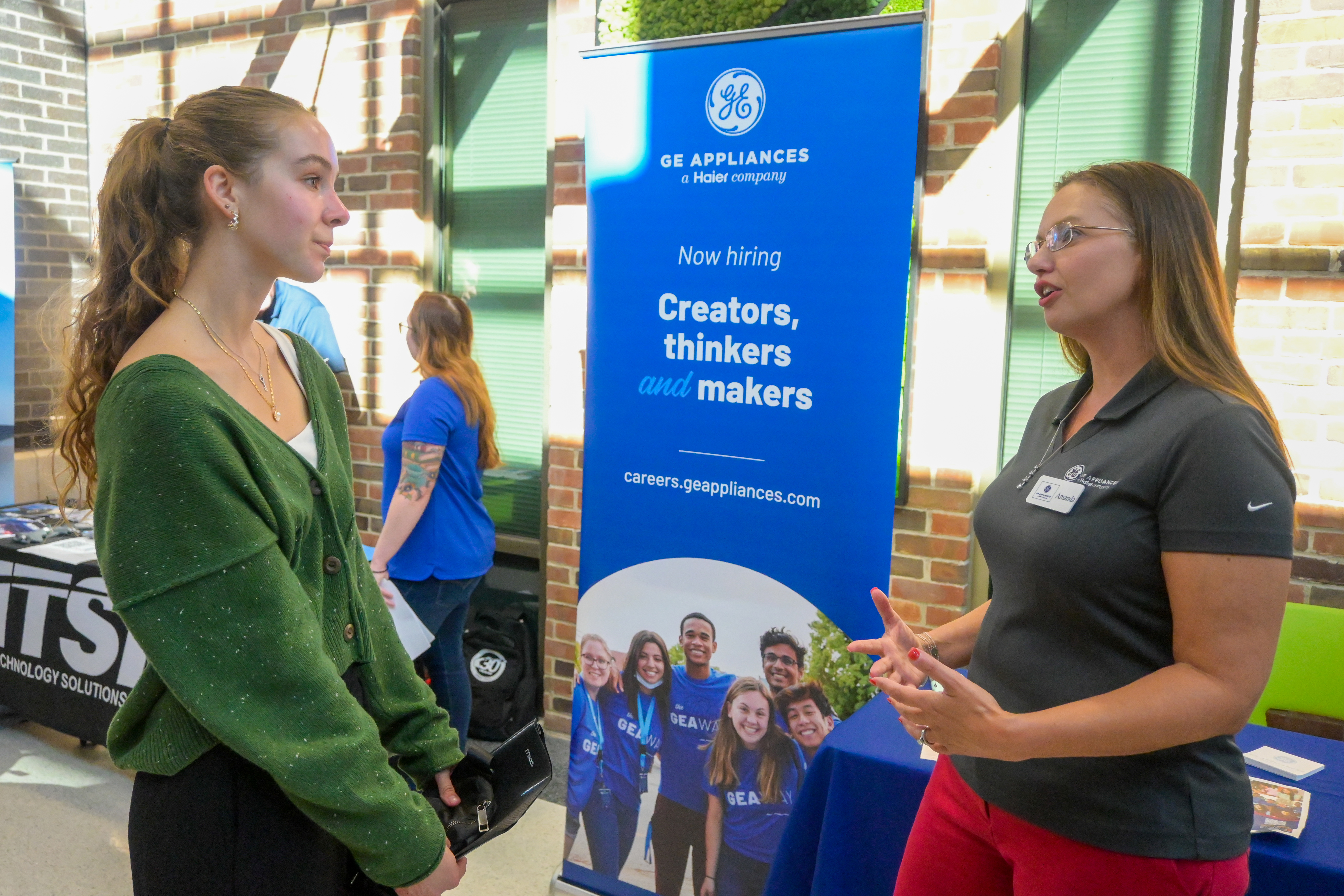 A female student in a green sweater talking to a female recruiter in a gray shirt.