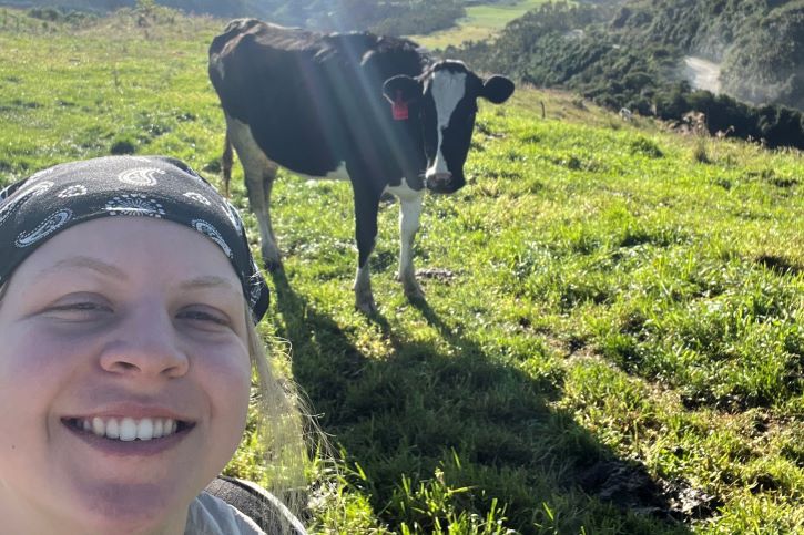 Jenna outside in the field with cow in the background