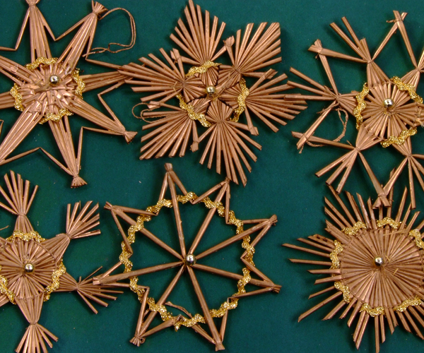 Set of eight straw ornaments in various star shapes. Each one has been painted gold and features a gold bead at the center and gold glitter ribbon woven into and glued to it. A hand-tied piece of string at the top allows each to hang on a Christmas tree.