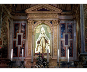 Statue of Mary shown in the altar outlined by golden, greek architecture. She has a light shining over her as she envelops multiple children under her cloak. 