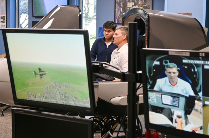 Computer monitors with images of test pilot in sim and student aircraft in flight
