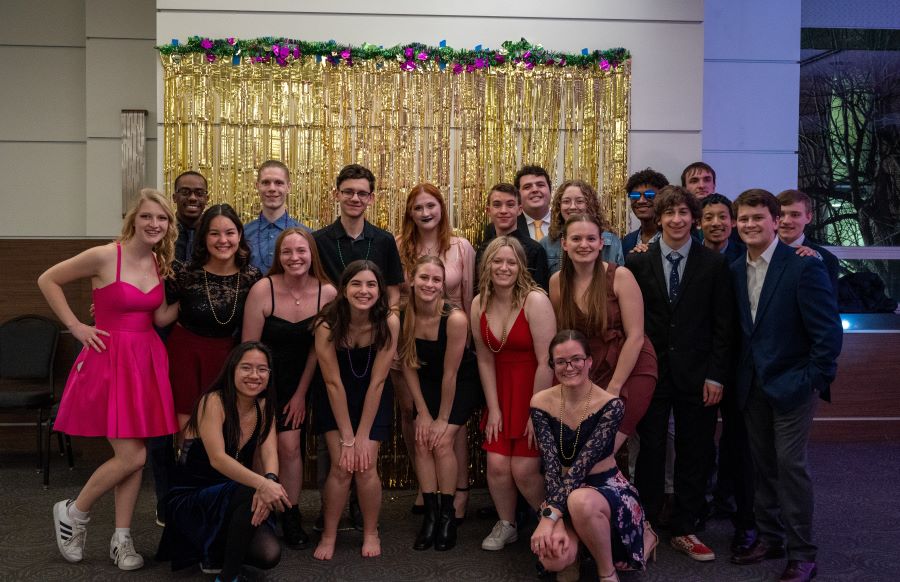 Large group of students posing in front of  Mardi Gras themed back drop