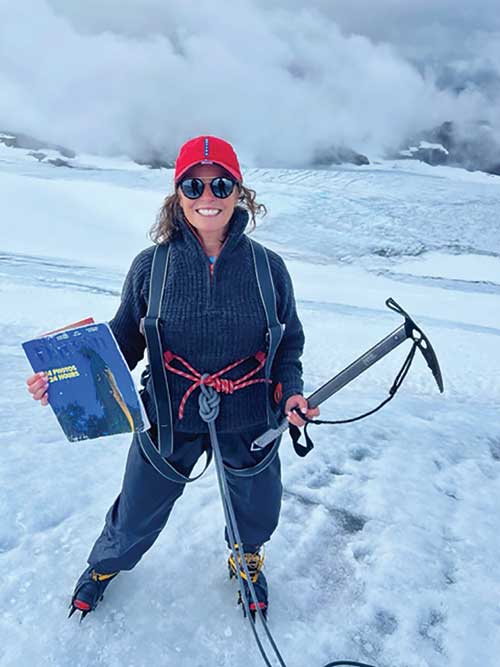 Alumna stands on glacier with a pick axe holding the magazine.